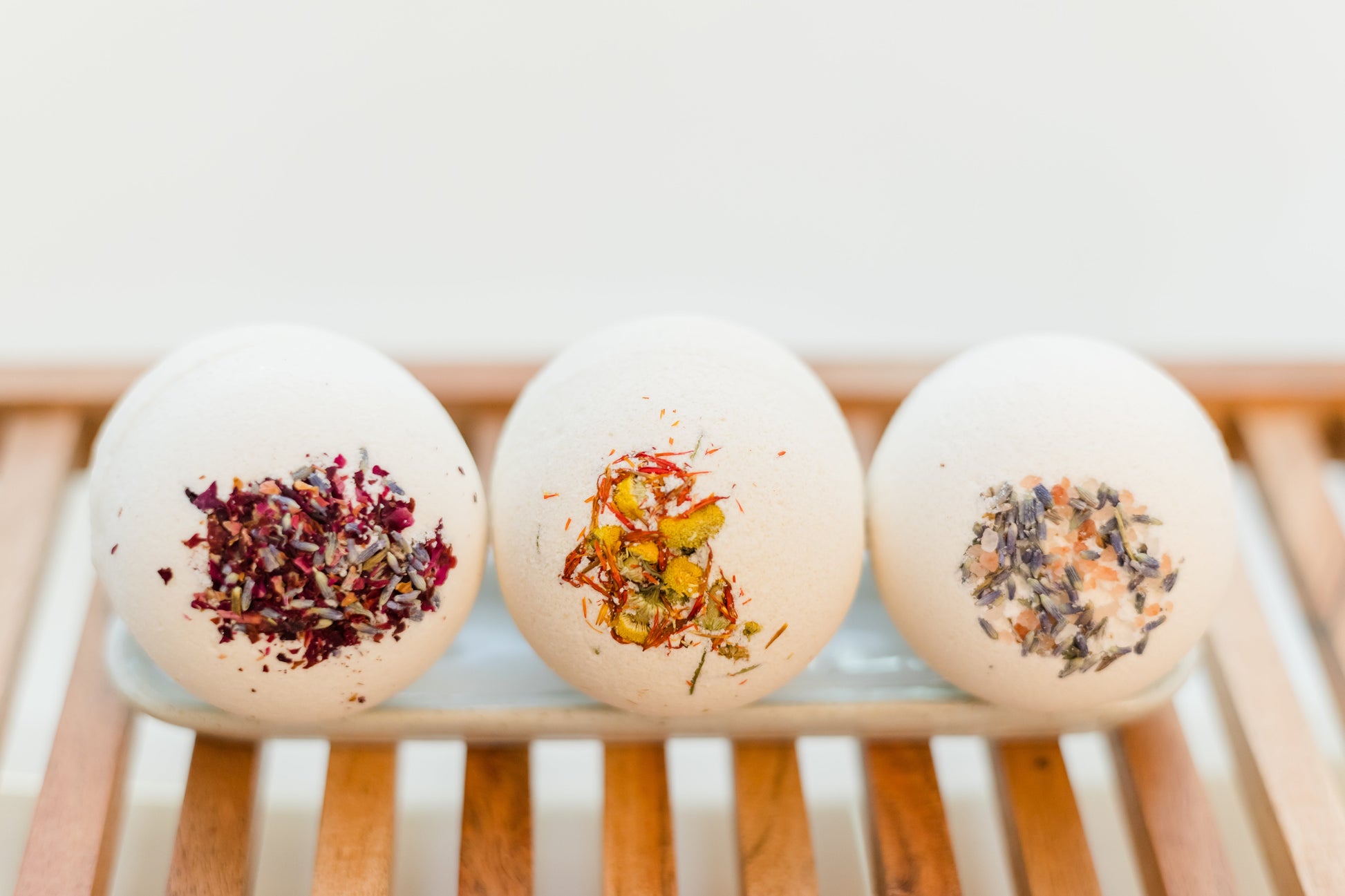 three large bath bombs with herbs embedded in them grouped together on a oval dish placed on a wooden bathtub rack