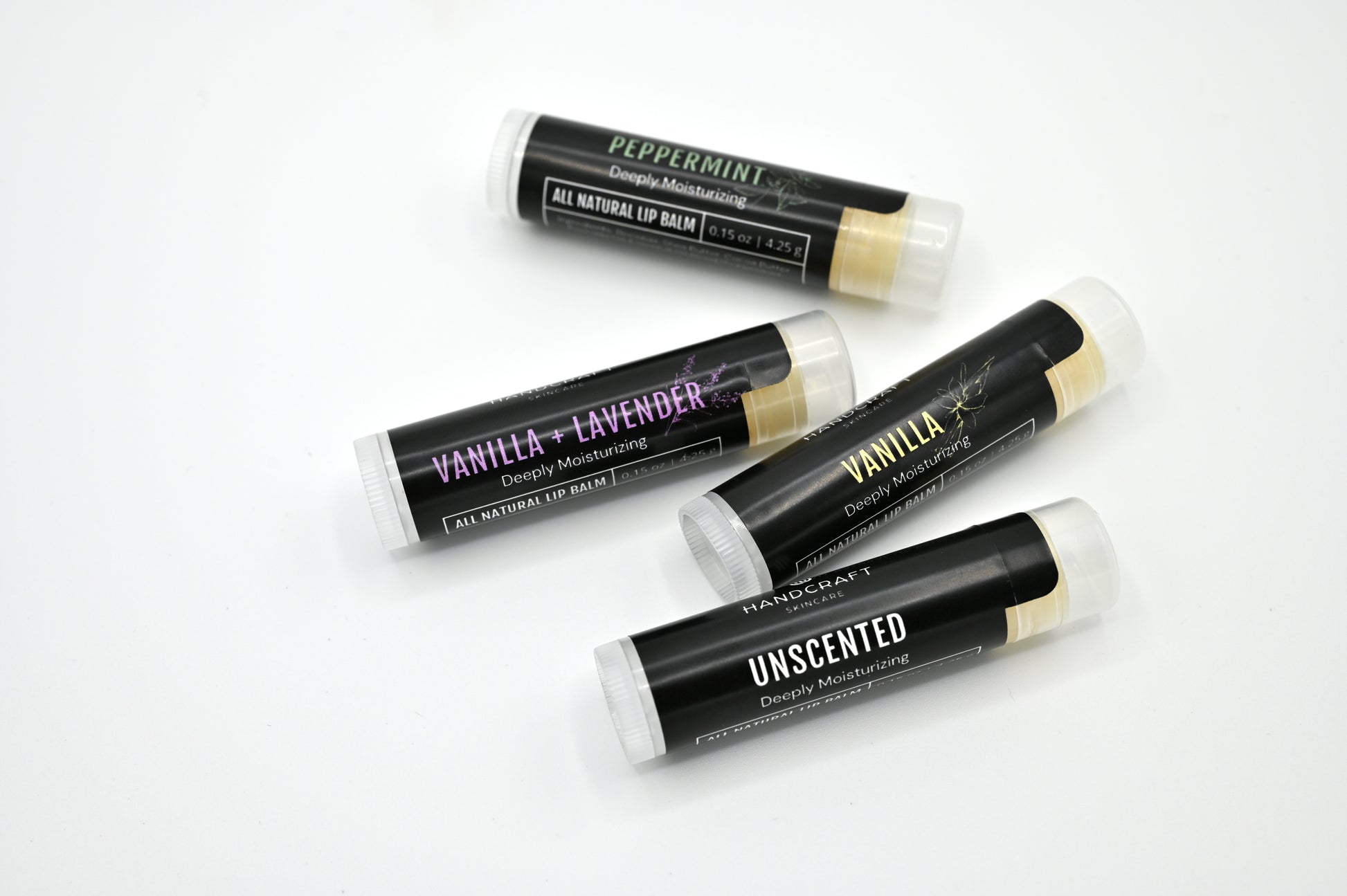 4 all natural lip balms with black labels laying on their side with a white background