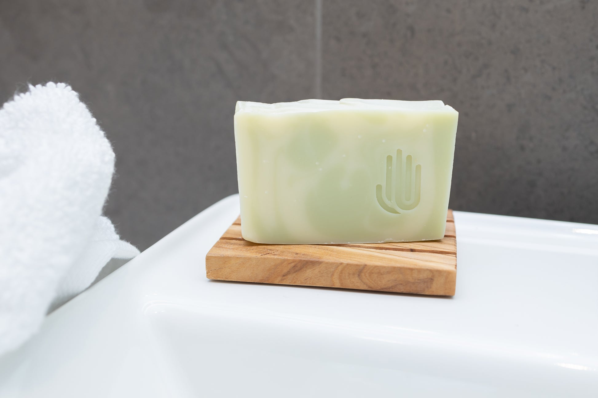 square white and green swirled soap on a wooden soap dish sitting on the edge of a white sink