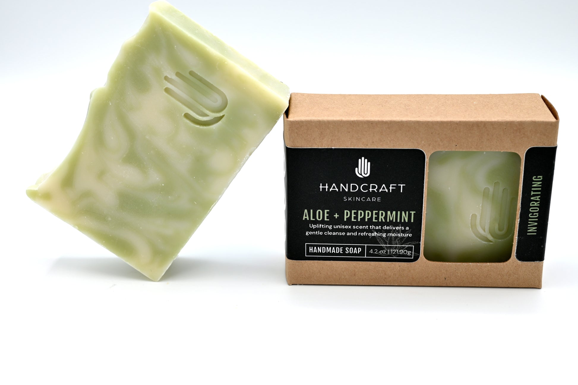green and white swirled aloe soap is unpackaged and leaning at an angle on a packaged aloe soap in a Kraft box with a black label
