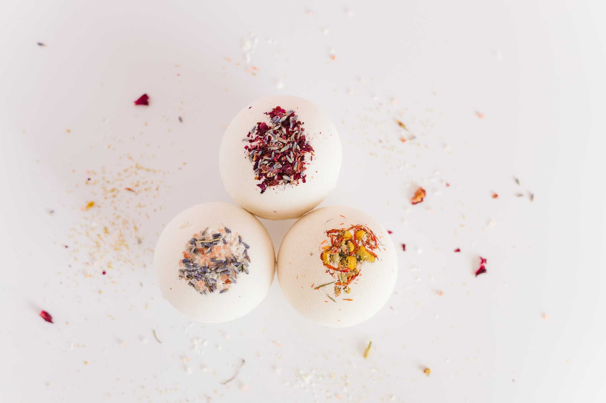 three large bath bombs with dried flowers embedded in them grouped together with dried flowers scattered around