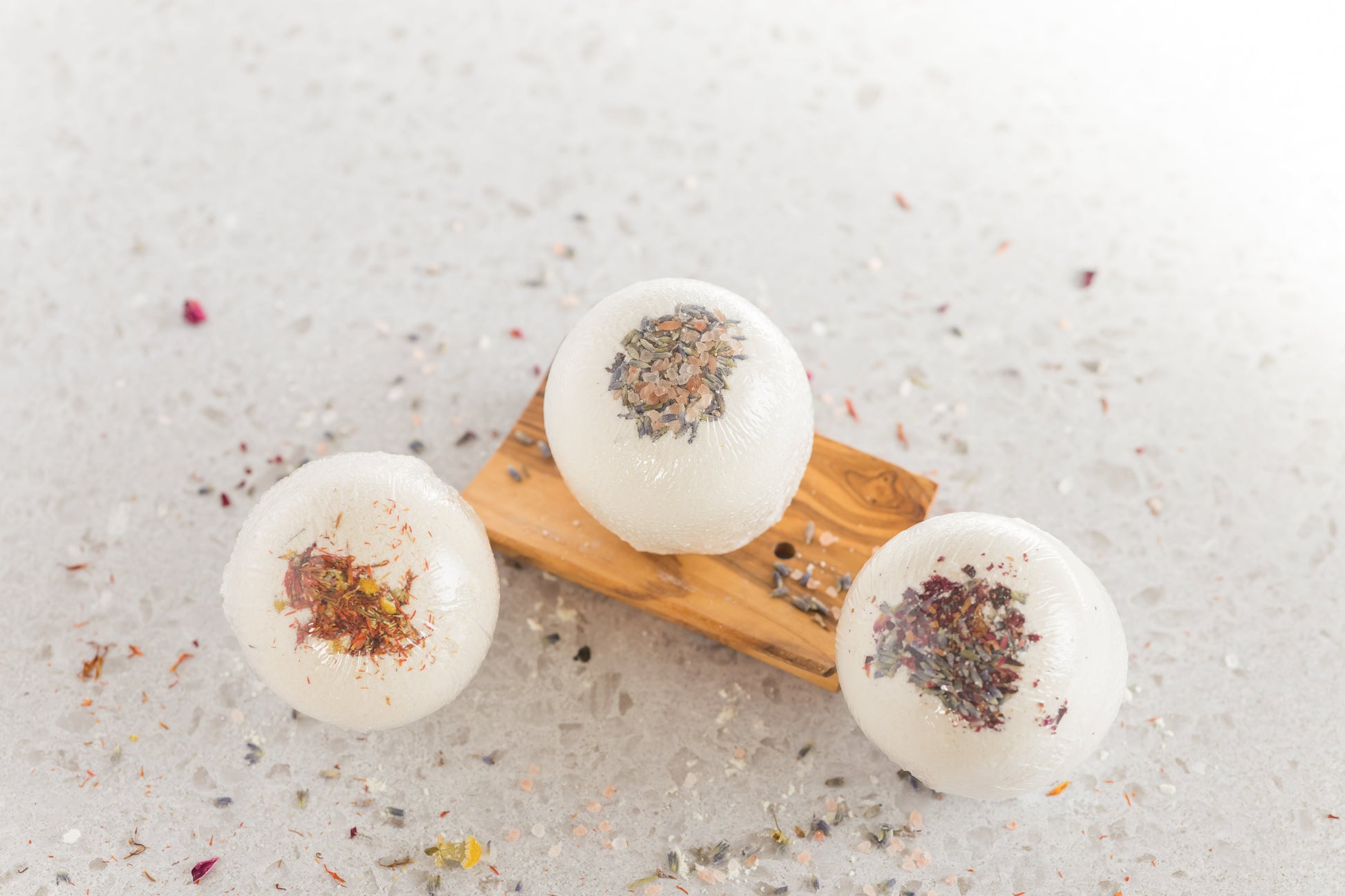 three large bath bombs with dried flowers embedded in them on a wooden dish with dried flowers scattered around