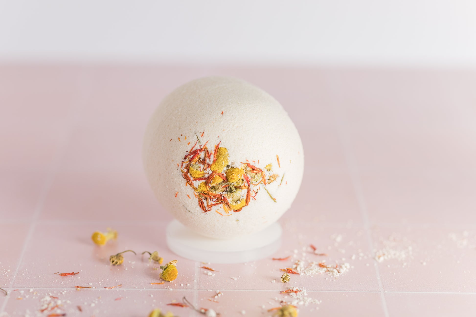 bath bomb on tile with dried chamomile buds and safflower petals scattered around it