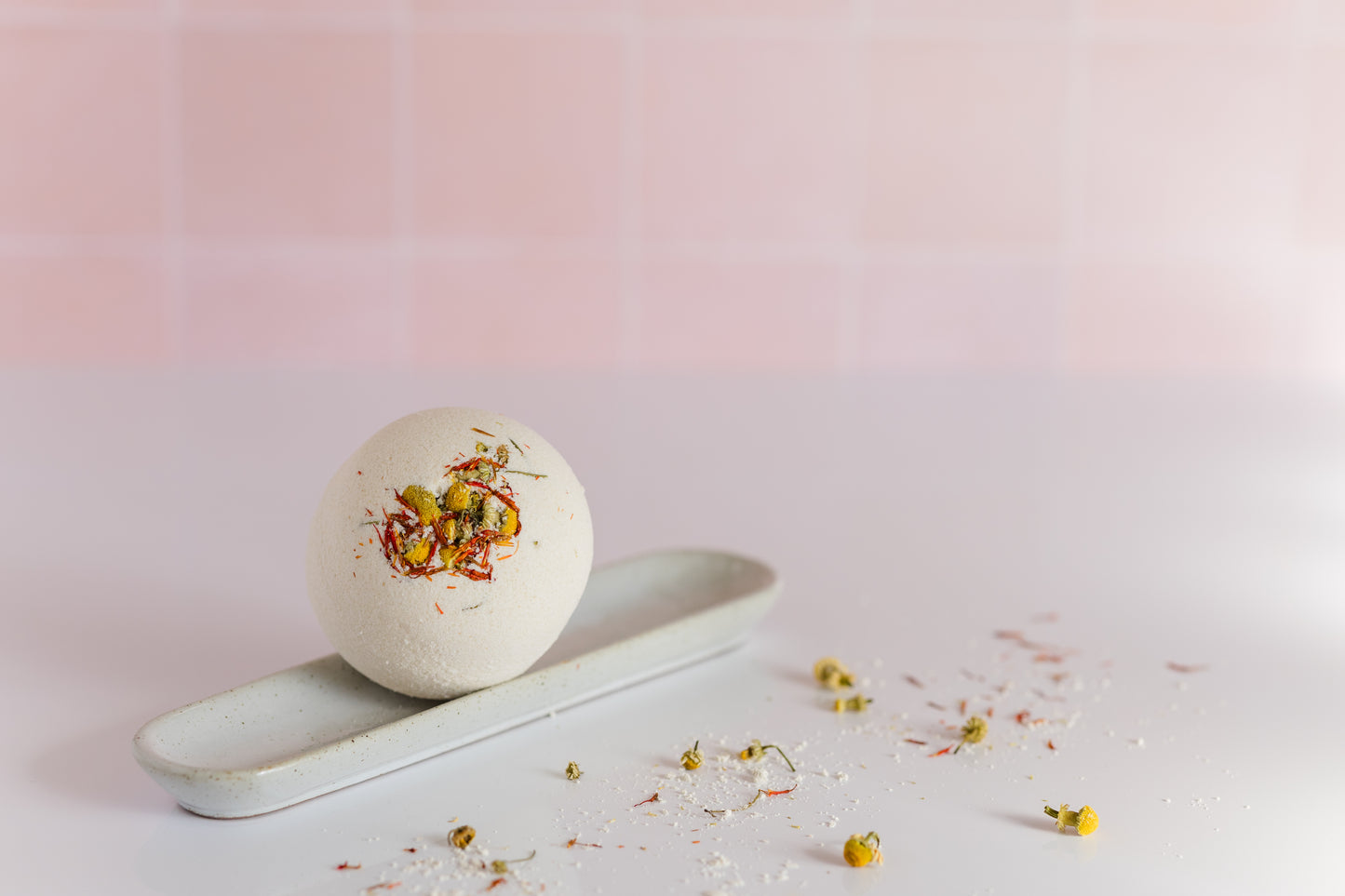 bath bomb on a circular plate with dried chamomile buds and safflower petals scattered around it