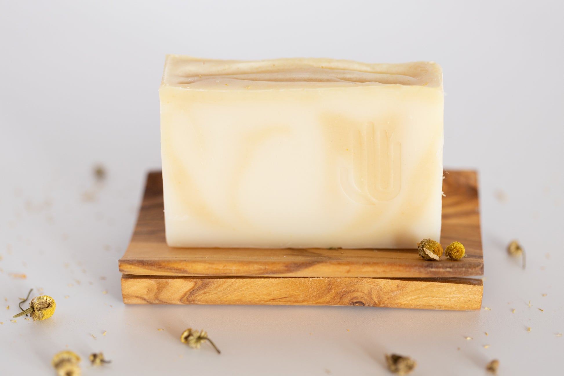 square white and yellow swirled soap sitting on a wood soap dish with chamomile buds sprinkled around