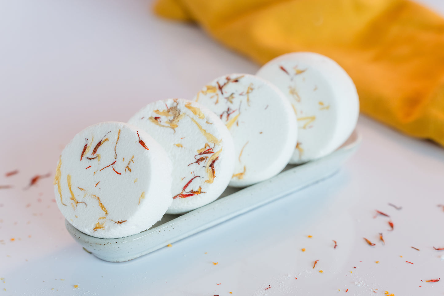 four citrus shower steamers on a ceramic tray with a yellow cloth behind it