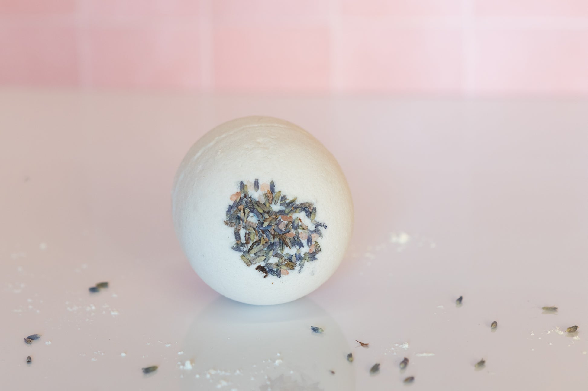 goat milk bath bomb on tile with lavender buds embedded in it and scattered around