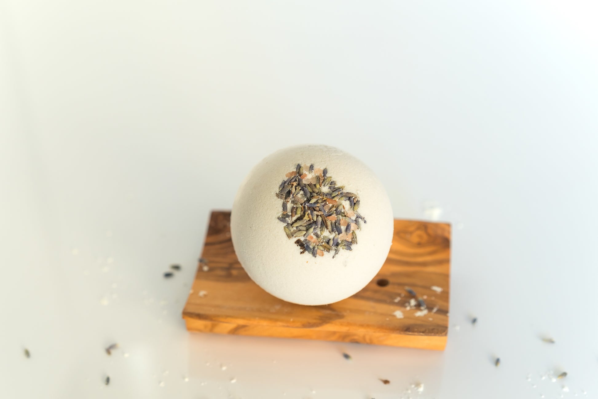 goat milk bath bomb on a wooden dish with lavender buds embedded in it and scattered around