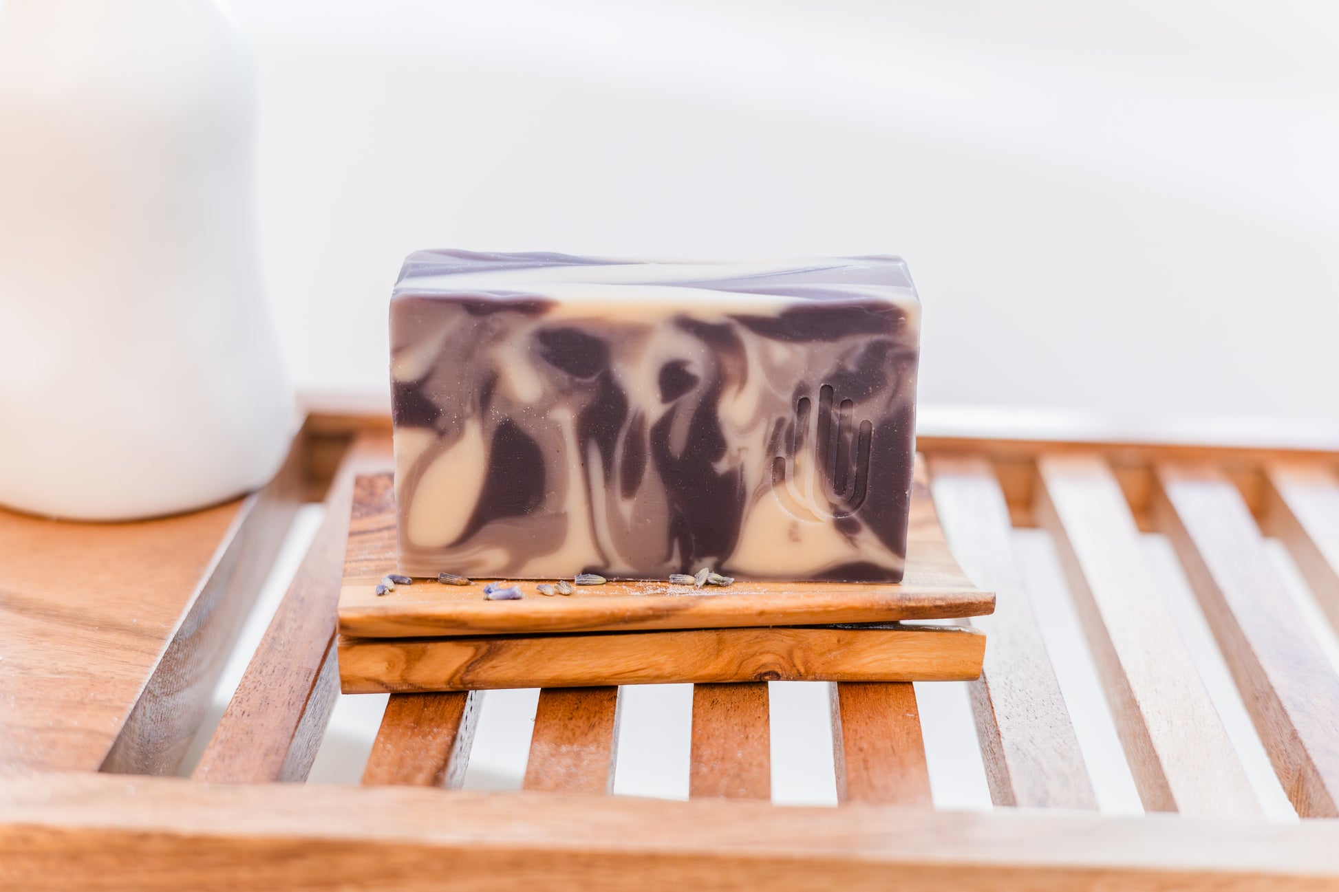 white purple and lavender swirled colored soap sitting on a wooden dish on a wooden bath shelf with lavender buds scattered around