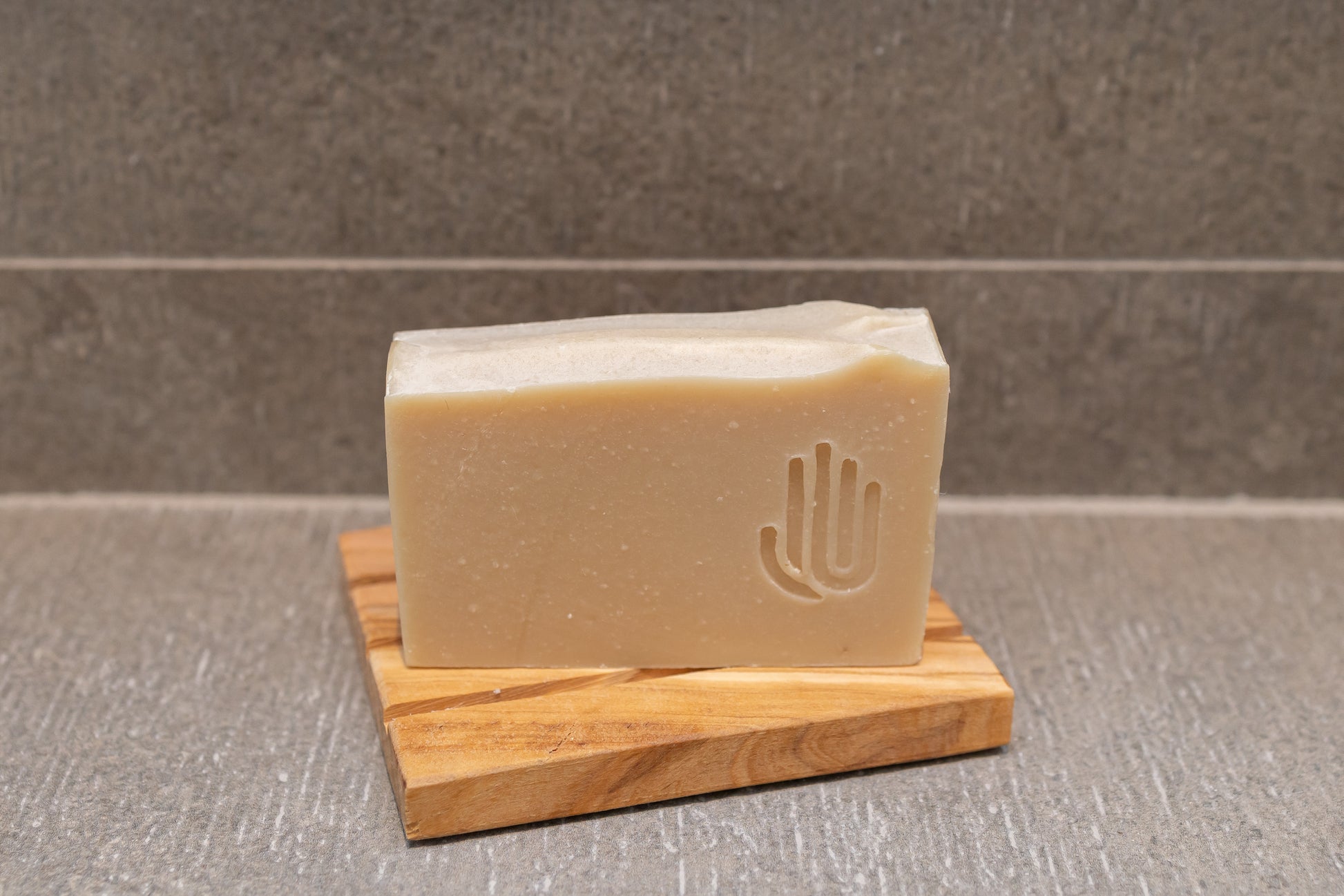 square tan colored soap on a wooden soap dish placed on shower tile