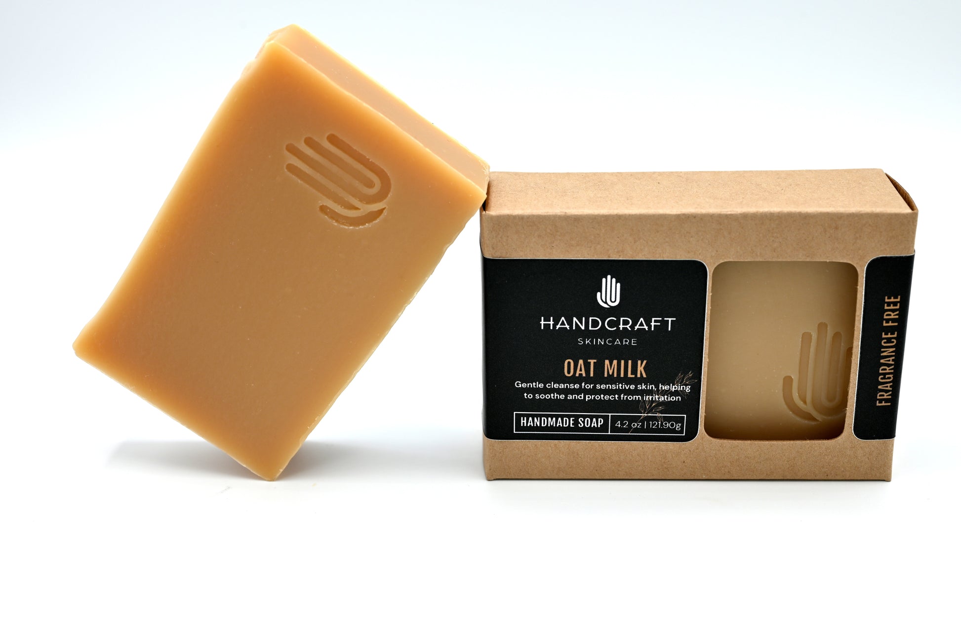 taupe colored oat milk soap is unpackaged and leaning at an angle on a packaged oat milk soap in a Kraft box with a black label