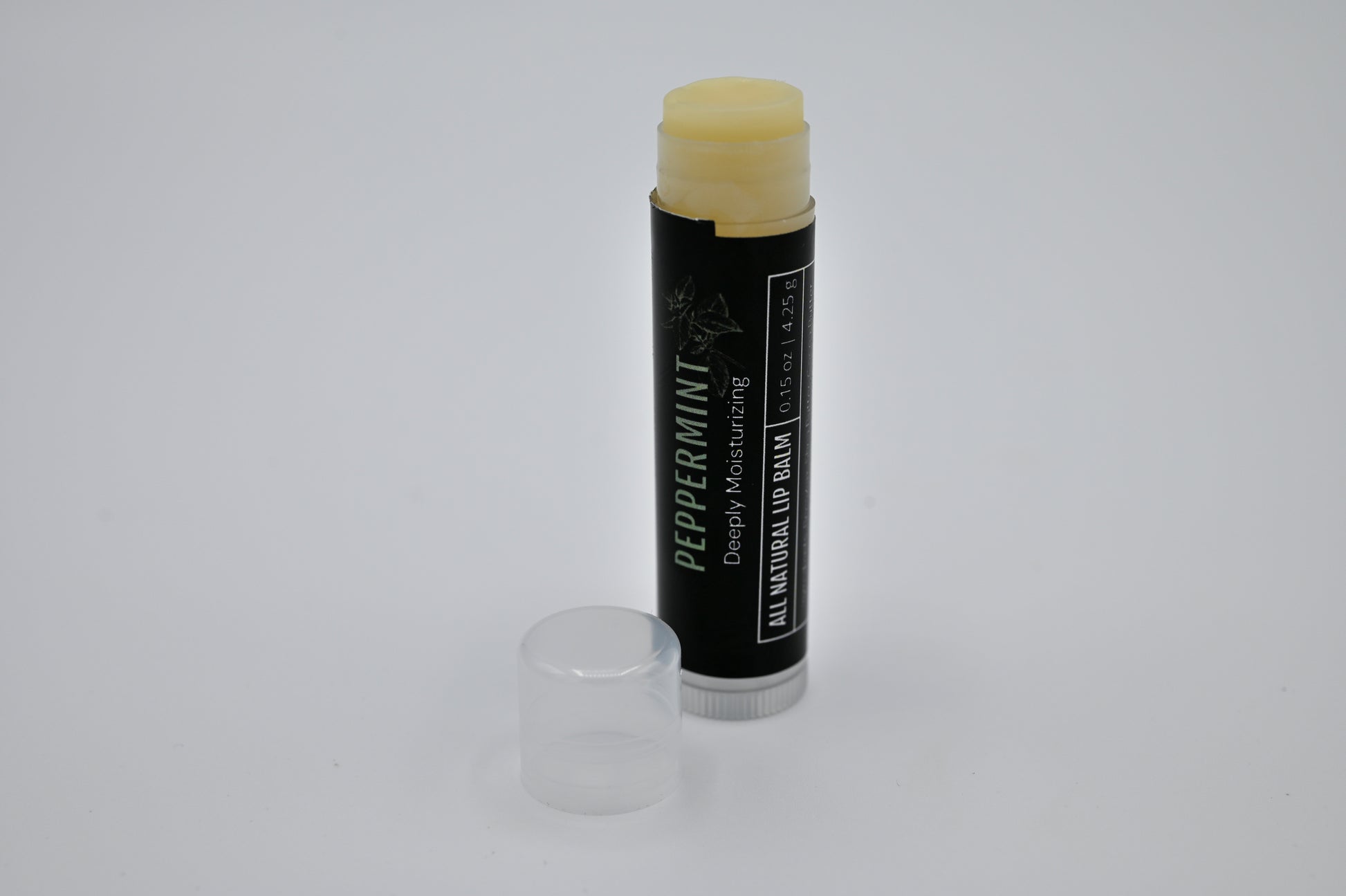 All natural peppermint lip balm with a black label with the container open showing a clear balm with a clear cap sitting to the side of the tube